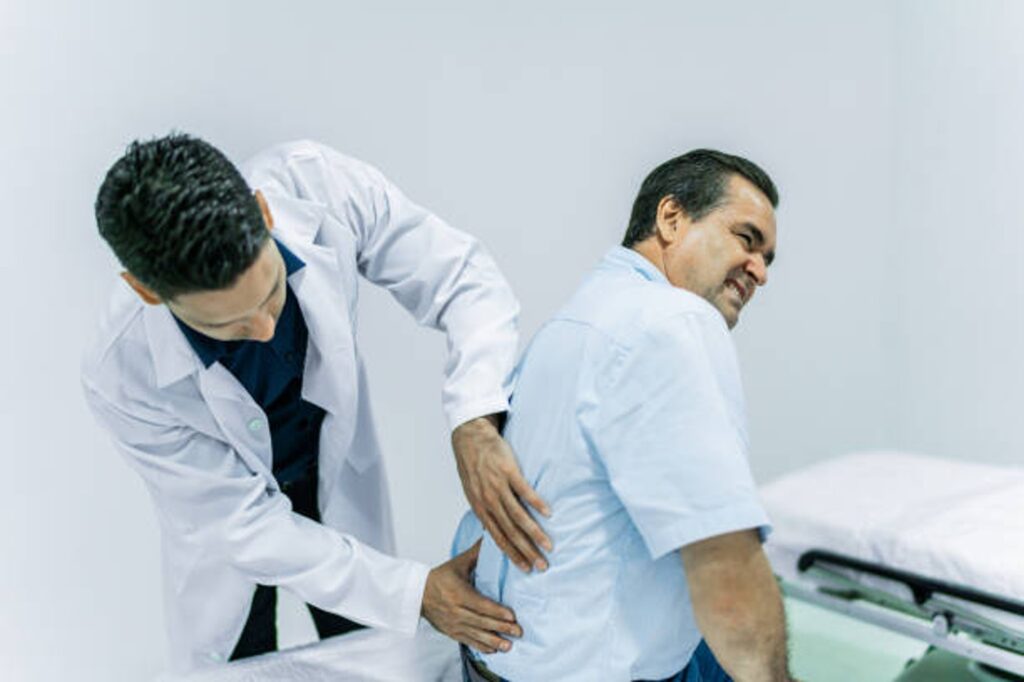 Two male doctors in white coats stand side by side, one placing a hand on the other's back in a clinical setting.