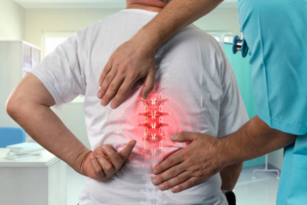 Healthcare provider palpates a patient’s lower back, with a red glow over the lumbar spine to indicate back pain.
